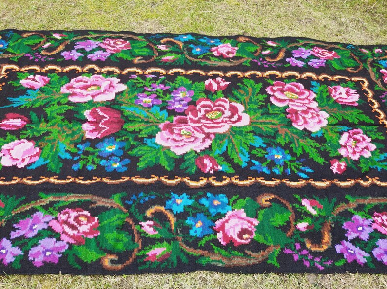 May include: A black wool rug with a floral pattern featuring pink, red, green, blue, and purple flowers. The rug has a gold border.