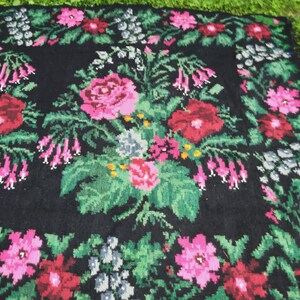 May include: A black wool rug with a floral pattern. The rug features pink, red, and green flowers on a black background.