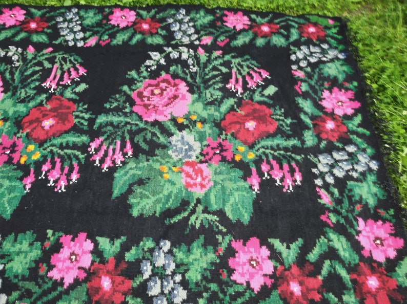 May include: A black wool rug with a floral pattern. The rug features pink, red, and green flowers on a black background.