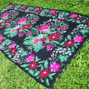 May include: A black rug with a floral pattern featuring pink, red, and green flowers. The rug has a fringed edge.