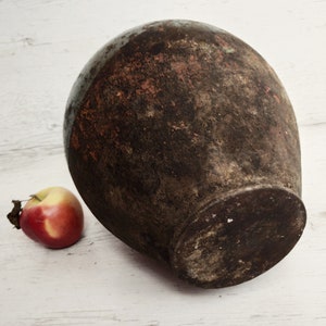 May include: A large, round, terracotta vase with a dark brown glaze and a rough, textured surface. The vase is sitting on a white wooden surface.
