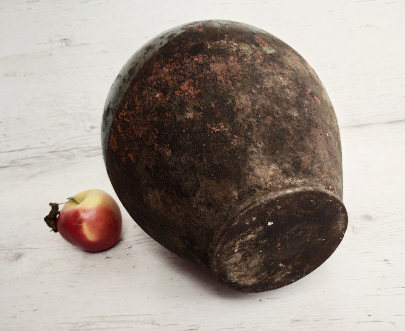 May include: A large, round, terracotta vase with a dark brown glaze and a rough, textured surface. The vase is sitting on a white wooden surface.