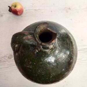 May include: A green glazed ceramic jug with a handle and a chipped opening. The jug has a rustic, aged appearance.