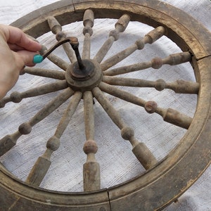 May include: A large, wooden spinning wheel with a circular frame and spokes. The wheel is made of natural wood and has a rustic appearance. The spokes are connected to a central hub, and the wheel is designed for spinning yarn.