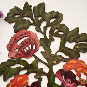 Peut inclure: Une d&eacute;coupe de papier d&eacute;corative repr&eacute;sentant un motif floral avec des fleurs rouges, roses et orange et des feuilles vertes. La d&eacute;coupe est peinte et a un aspect rustique et vintage.