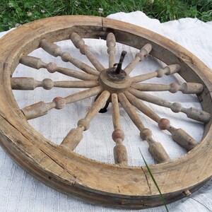 May include: A large, wooden spinning wheel with a circular frame and spokes radiating from the center. The wheel is made of natural wood and has a rustic, antique appearance.