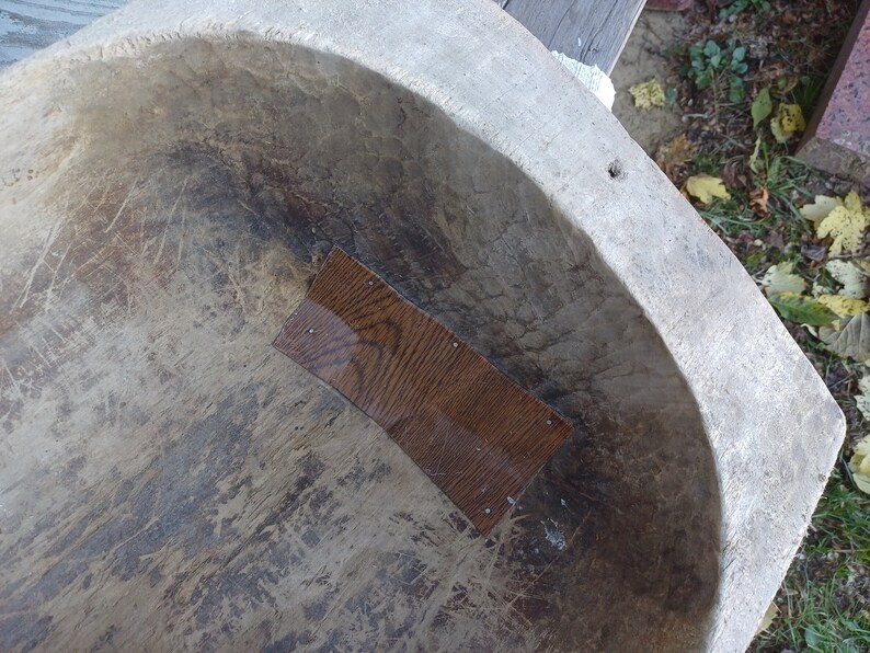 May include: A large, oval-shaped wooden bowl with a worn, gray surface. The bowl has a rectangular patch of wood on the inside, which is a darker brown color.