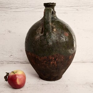 May include: A large, green and brown ceramic jug with a handle. The jug has a rough, textured surface and appears to be very old.