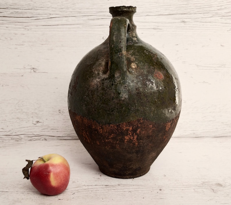 May include: A large, green and brown ceramic jug with a handle. The jug has a rough, textured surface and appears to be very old.