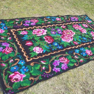 May include: A black rug with a floral pattern. The rug features pink, blue, and green flowers on a black background. The rug has a gold border.