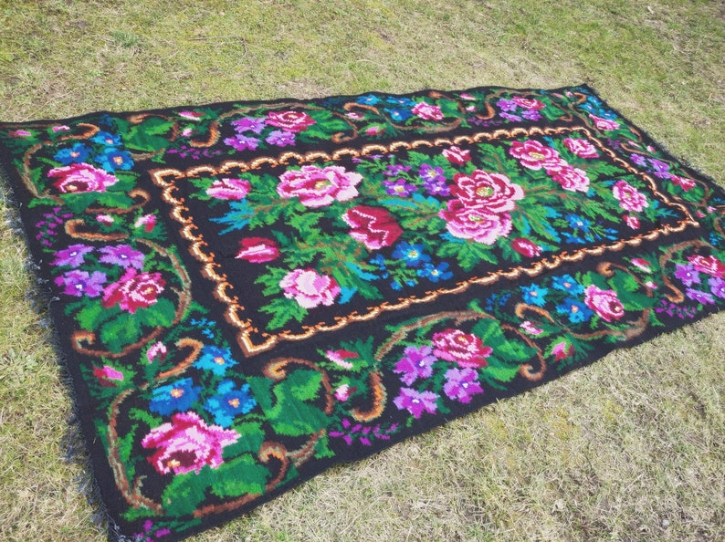 May include: A black rug with a floral pattern. The rug features pink, blue, and green flowers on a black background. The rug has a gold border.