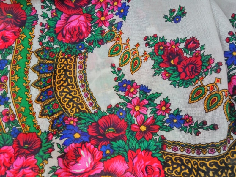 K&ouml;nnte beinhalten: Wei&szlig;er Stoff mit einem bunten Blumenmuster. Das Muster zeigt rote, rosa, blaue, gr&uuml;ne und gelbe Blumen. Der Stoff hat ein sich wiederholendes Muster aus verzierten goldenen und schwarzen Designs.