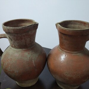 May include: Two brown clay jugs with handles. The jugs are slightly different in size and shape.