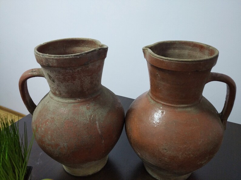 May include: Two brown clay jugs with handles. The jugs are slightly different in size and shape.