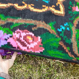 May include: A black wool rug with a floral pattern. The rug features pink, purple, green, and orange flowers on a black background.