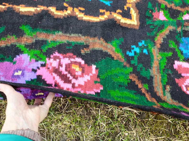 May include: A black wool rug with a floral pattern. The rug features pink, purple, green, and orange flowers on a black background.