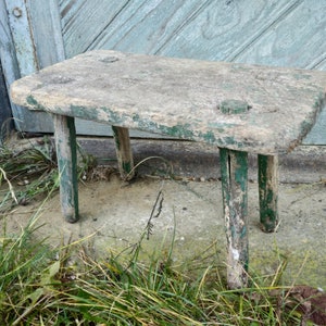 Puede incluir: Un taburete de madera r&uacute;stico con un acabado de pintura verde desgastada. El taburete tiene cuatro patas y una parte superior rectangular.