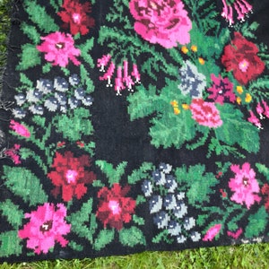 May include: A black rug with a floral pattern. The rug features pink, red, and green flowers on a black background. The rug has a fringe border.
