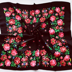 May include: A black square scarf with a floral pattern of red, pink, and green roses. The scarf is folded in half and has a textured surface.
