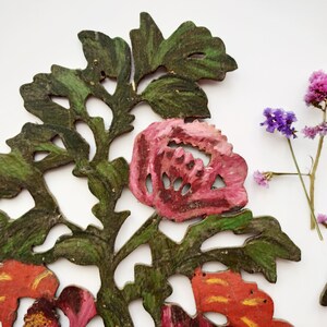 Peut inclure: Ensemble de trois d&eacute;corations murales florales. Les pi&egrave;ces sont en bois et peintes dans des tons de vert, rose et orange. Les fleurs sont stylis&eacute;es et ont un aspect vintage.