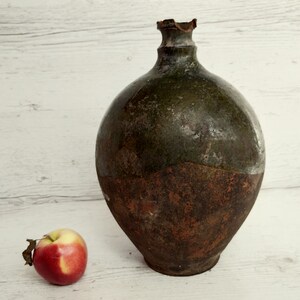 May include: A large, round, green and brown ceramic jug with a chipped rim. The jug has a rustic, aged appearance.