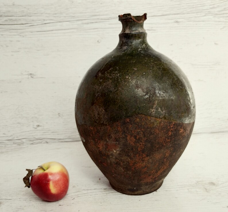 May include: A large, round, green and brown ceramic jug with a chipped rim. The jug has a rustic, aged appearance.
