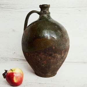May include: A large, green and brown ceramic jug with a handle. The jug has a rustic, aged appearance.