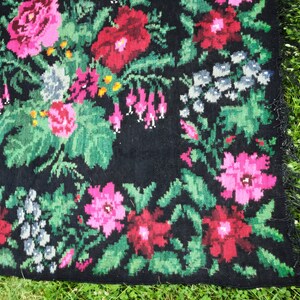 May include: A black rug with a floral pattern. The rug is woven with pink, red, and green flowers on a black background.