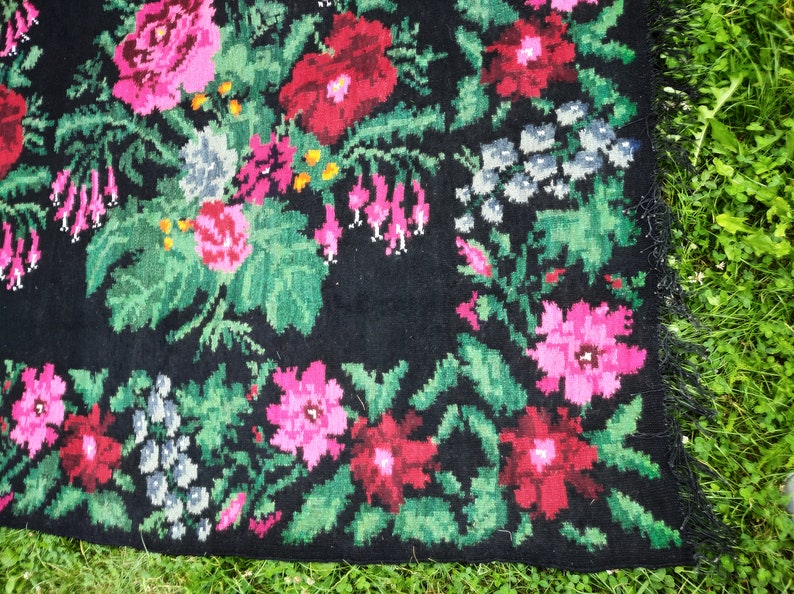 May include: A black rug with a floral pattern. The rug is woven with pink, red, and green flowers on a black background.