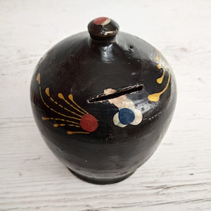Könnte beinhalten: Schwarzes Keramik-Sparschwein mit goldenen und roten bemalten Designs. Das Sparschwein hat einen Schlitz an der Seite für Münzen.