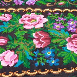 May include: A close-up of a colourful woven rug with a floral pattern. The rug features pink, red, blue, and green flowers on a black background.
