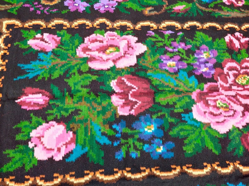 May include: A close-up of a colourful woven rug with a floral pattern. The rug features pink, red, blue, and green flowers on a black background.