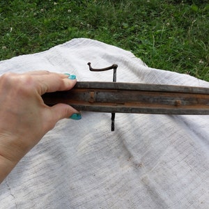 May include: A wooden wheel rim with metal spokes and nails. The rim is brown and weathered, and the spokes are rusty. The wheel is being held by a hand with blue nail polish.