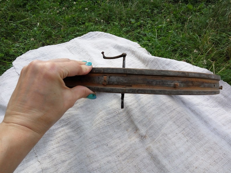 May include: A wooden wheel rim with metal spokes and nails. The rim is brown and weathered, and the spokes are rusty. The wheel is being held by a hand with blue nail polish.