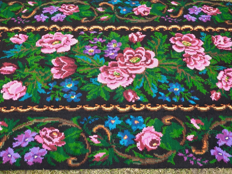 May include: A traditional Romanian rug with a floral pattern. The rug is woven with wool and features a black background with pink, red, blue, and green flowers.