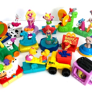 May include: A collection of 14 colorful plastic toy characters from the Happy Meal toy line. The toys include characters like Ariel from The Little Mermaid, ET, a Dalmatian, a pink ballerina, a green frog, a red bird, a yellow truck, and a purple television. The toys are all connected together in a train-like formation.