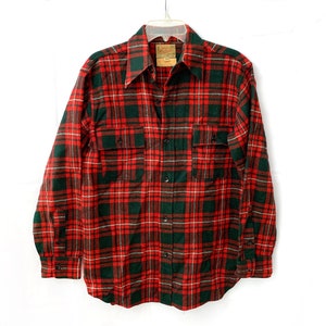 May include: Red and green plaid flannel shirt with a button-up front and long sleeves. The shirt has two chest pockets.