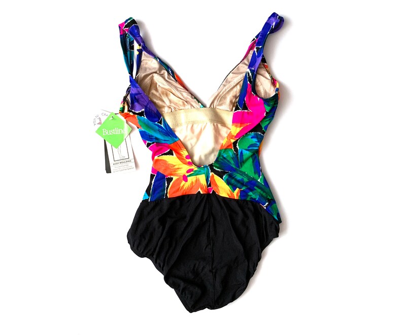 May include: A black swimsuit with a colorful floral print. The swimsuit has a deep V-neckline and a low back. The print features pink, yellow, green, blue, and purple flowers.