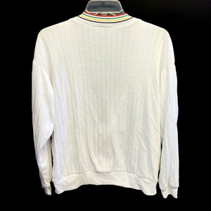 Pode incluir: Camisola branca de manga comprida com textura canelada e gola listrada colorida.