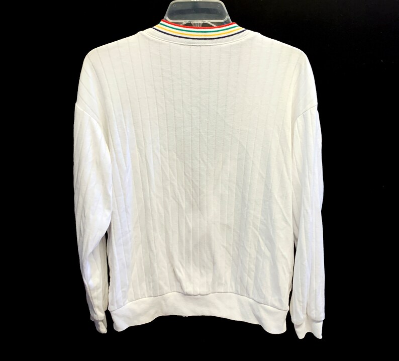 Pode incluir: Camisola branca de manga comprida com textura canelada e gola listrada colorida.