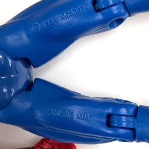 以下が含まれることがあります： 1994 MARVEL CHINAとTOY BIZ INC.という刻印がある青いプラスチック製のアクションフィギュアの脚部。関節部分があり、一部に赤と黒の模様が施された表面が見える。フィギュアのパーツは青いプラスチック素材で構成されている。