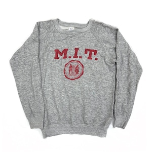 Puede incluir: Una sudadera gris jaspeada con las letras "M.I.T." en rojo sobre un emblema circular rojo. La sudadera tiene cuello redondo y mangas largas.