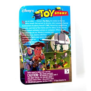 May include: A close-up of the back of a Toy Story trading card featuring Woody and Buzz Lightyear. The card is blue and green with the text "Disney's Toy Story" in white. The card also features a picture of Woody and Buzz Lightyear in a scene from the movie. The card is numbered 5.