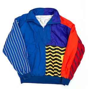 K&ouml;nnte beinhalten: Eine farblich abgesetzte Adidas-Pulloverjacke mit blauem Hauptteil, violettem Oberteil und rotem &Auml;rmel. Der linke &Auml;rmel hat wei&szlig;e vertikale Streifen, w&auml;hrend das untere rechte Feld ein gelb-schwarzes Wellenmuster aufweist. Sie hat einen hohen Kragen.