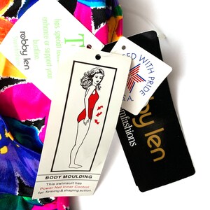 May include: A multi-colored swimsuit with a black and white geometric pattern. The swimsuit has a tag that says "Body Moulding" and "Power Net Inner Control for firming & shaping action". The tag also has a drawing of a woman wearing a red swimsuit.
