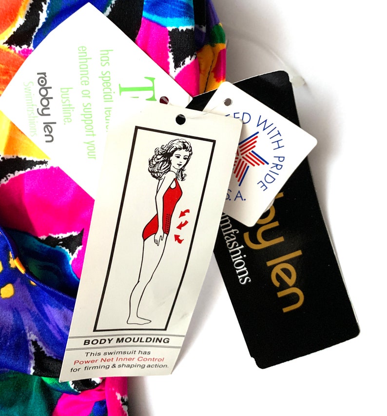 May include: A multi-colored swimsuit with a black and white geometric pattern. The swimsuit has a tag that says "Body Moulding" and "Power Net Inner Control for firming & shaping action". The tag also has a drawing of a woman wearing a red swimsuit.