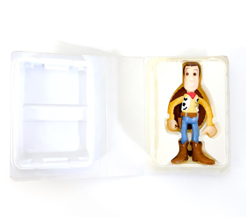 May include: A plastic toy figure of Woody from Toy Story. Woody is wearing his signature brown vest, yellow shirt, and blue jeans. He is holding his sheriff's badge and has a friendly expression on his face.