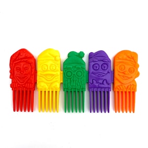 May include: Six colorful plastic hair combs with cartoon faces. The combs are red, yellow, green, purple, orange, and blue.