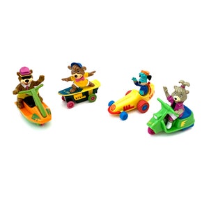 Pode incluir: Quatro figuras de brinquedo de plástico de personagens de desenhos animados a andar em diferentes veículos. Um urso castanho numa mota de água, um urso castanho num skate, um cão azul num carro de corrida e um urso castanho num scooter.