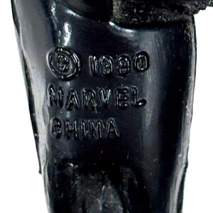 Pu&ograve; includere: Una gamba di action figure in plastica nera con testo stampato che recita &copy; 1990 MARVEL CHINA. La superficie &egrave; liscia e lucida, con le scritte in rilievo chiaramente visibili sul materiale scuro e solido del componente del giocattolo.